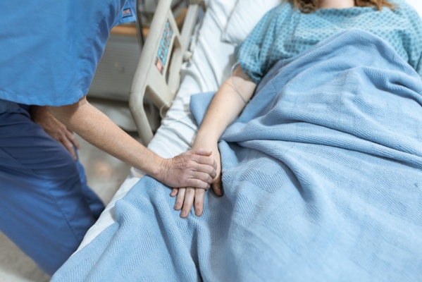 Person holding patients hand in hospital bed
