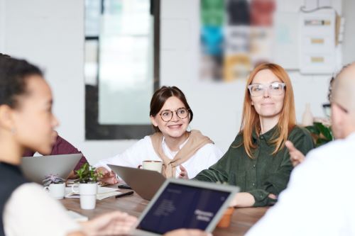 Photo of people around a table looking at laptops smiling