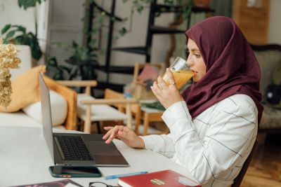 Photograph of young woman on a laptop having a drin